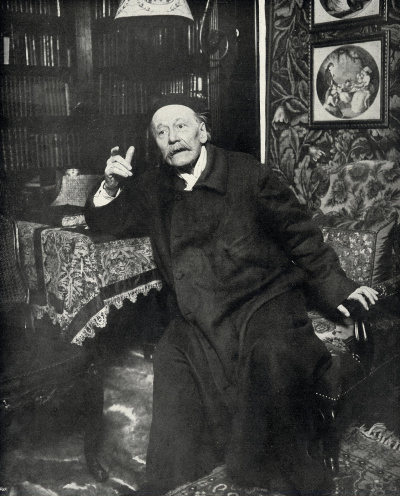 Jules Massenet assis accoudé à une table levant le doigt.<br>